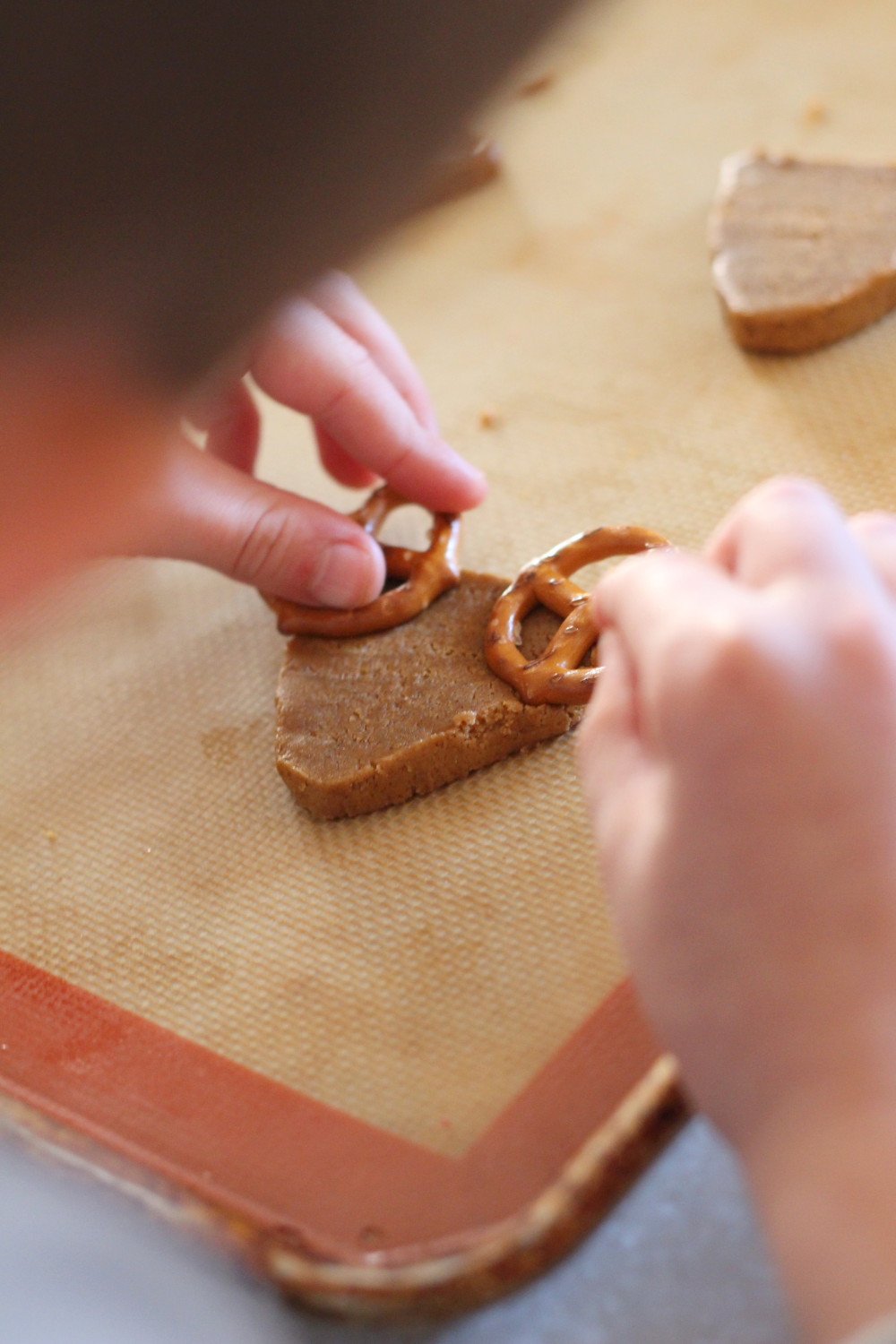 kid putting pretzel antlers on reindeer cookies