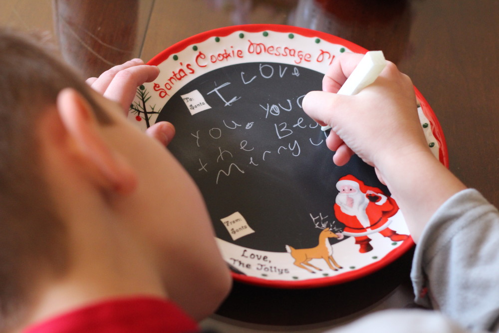 boy writing message to Santa on chalkboard plate