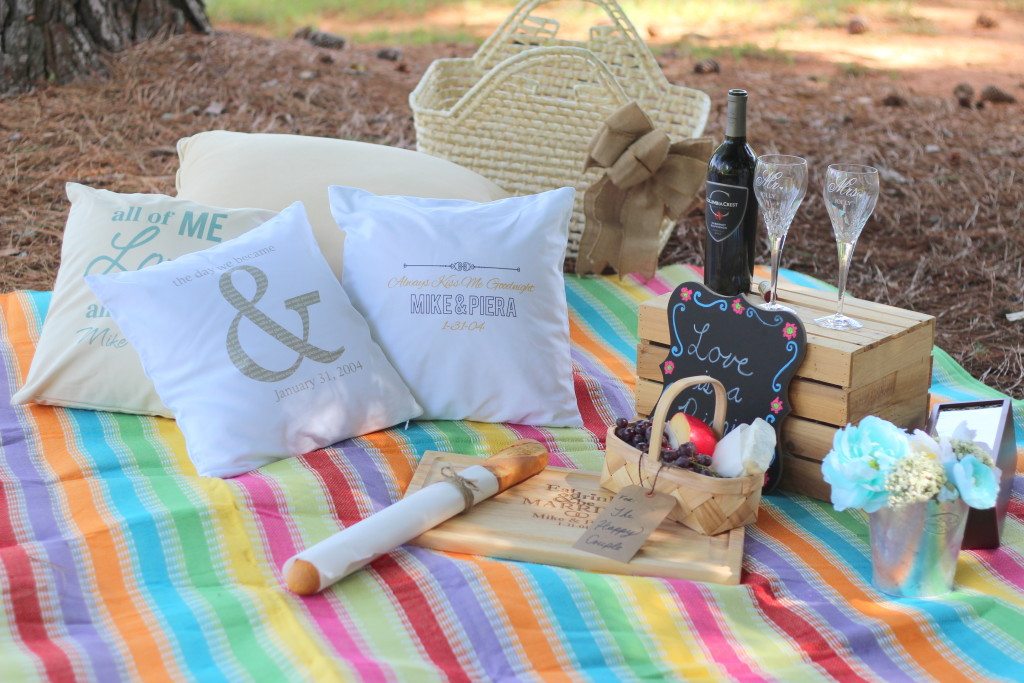 wine glasses on a box cutting board with cheese fruit and bread chalkboard and personalized pillows on a picnic blanket