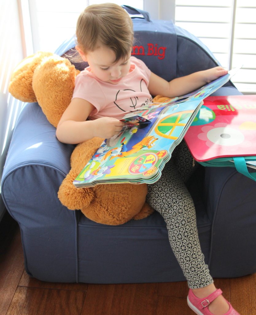 girl reading story book on chair and teddy bear