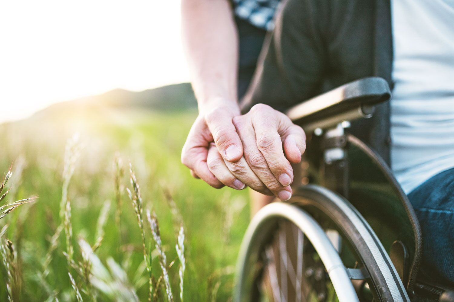 hand holding older man in wheelchair's hand in field 