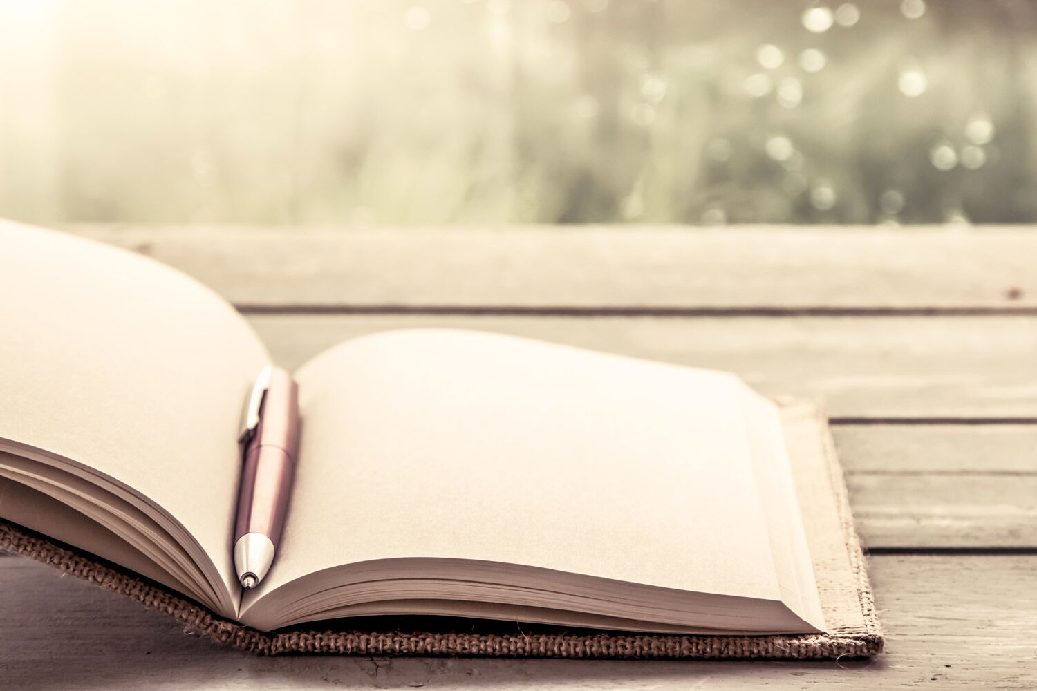 open notebook and pen laying on desk with rainy window in background