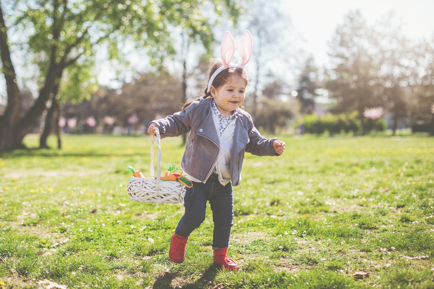 little girl with bunny ears running through field with easter basket